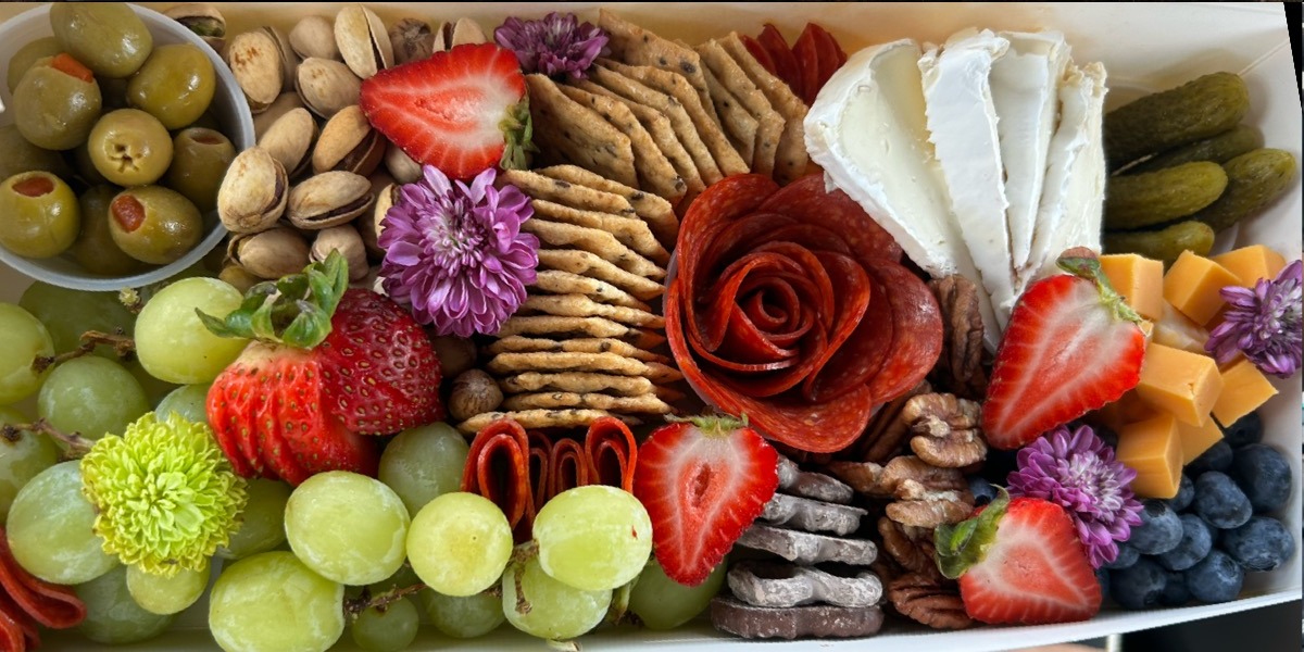 Long charcuterie box filled with cheeses, fruit, salami rose and flowers