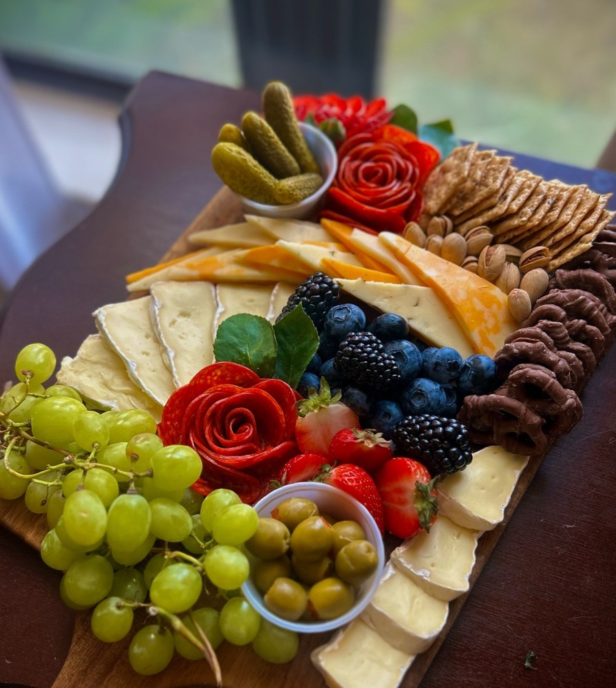 Wooden charcuterie board with brie, berries, grapes and a salami rose