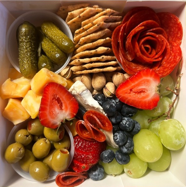 Open charcuterie box with salami rose, olives, fruit and crackers