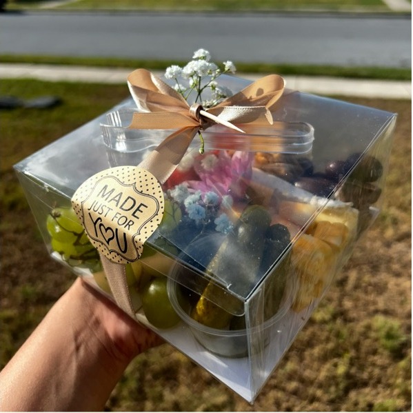 Clear gift box of charcuterie tied with a champagne ribbon